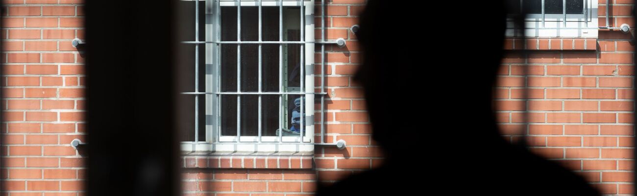 Ein Insasse steht vor einem vergitterten Fenster in der Abschiebehaftanstalt in Büren. Ein 17-Jähriger aus Serbien war hier ebenfalls untergebracht. (Archivfoto), © Friso Gentsch/dpa